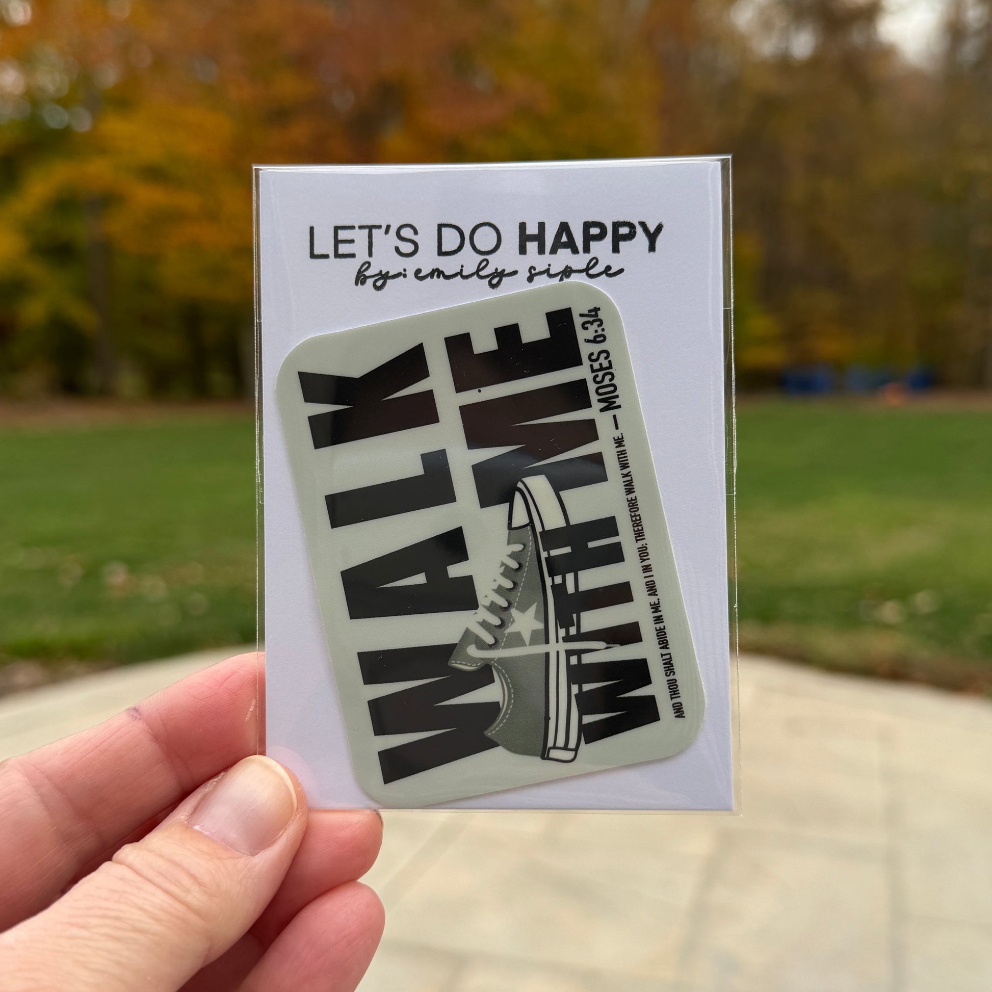 Hand holding a sticker with text against a blurred outdoor background